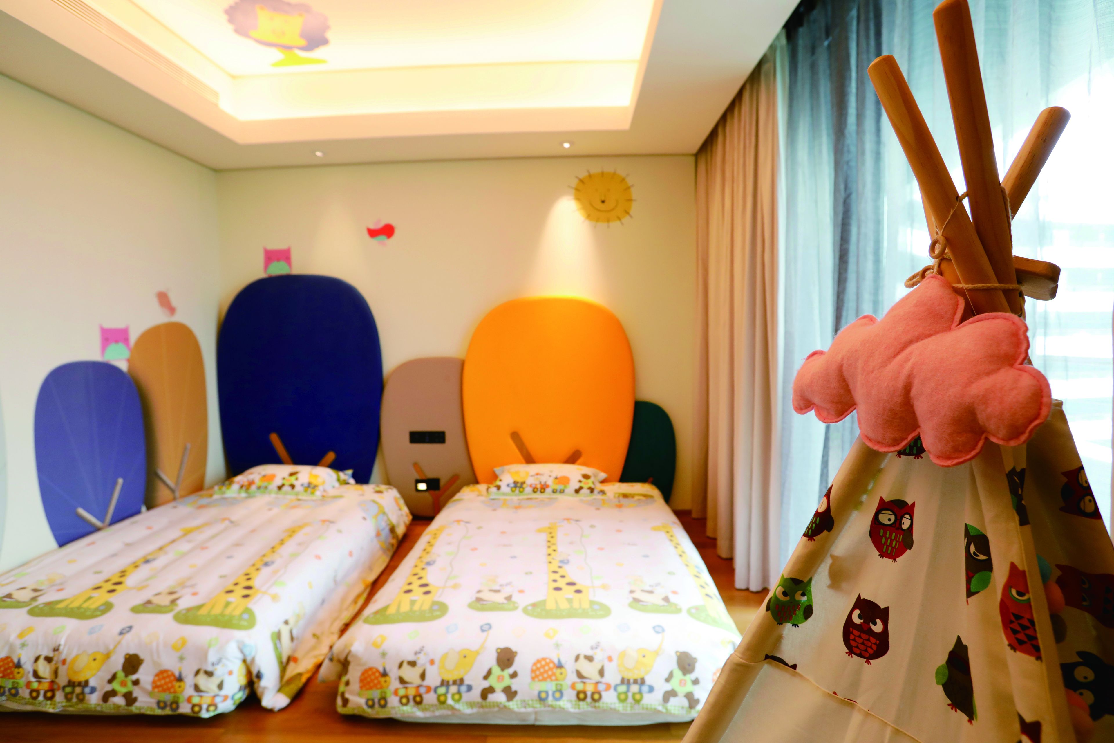Une chambre d’enfant avec deux lits, une fenêtre avec des rideaux et un jouet en peluche.