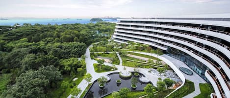 A modern hotel with a curved architecture, surrounded by lush greenery and a view of the sea.