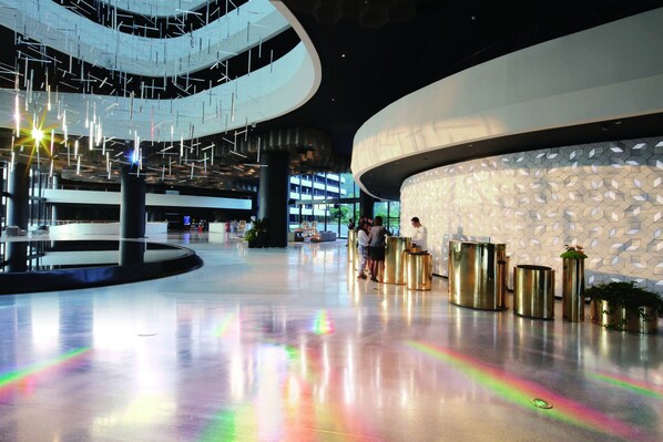 A spacious lobby with a modern design, featuring a curved wall with a geometric pattern and a central area with a reflective floor.