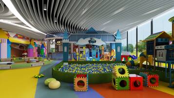 Un área de juegos infantiles con piscina de pelotas, estructuras de juego coloridas y un edificio grande con techo azul.