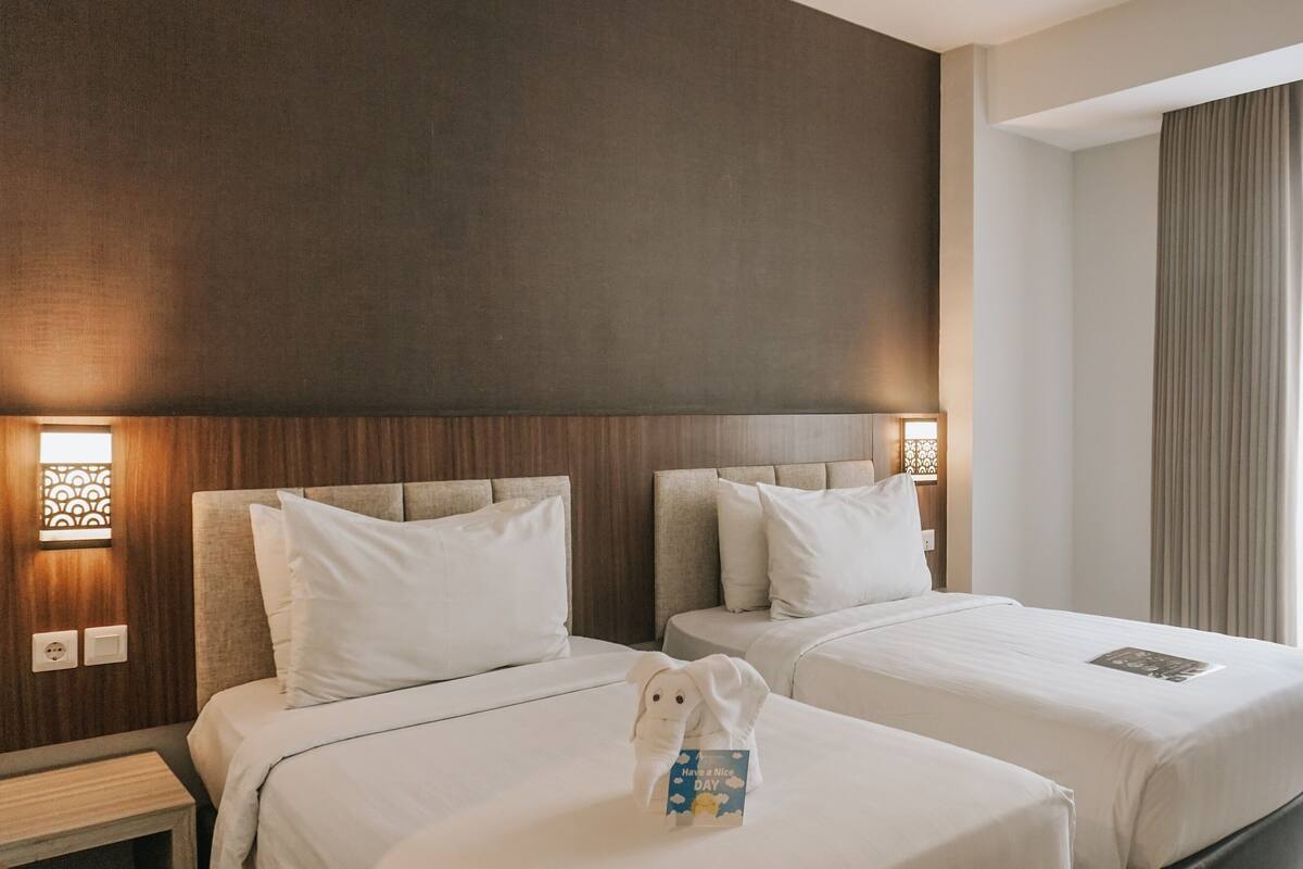 A hotel room with two beds, a nightstand, and a window with curtains.