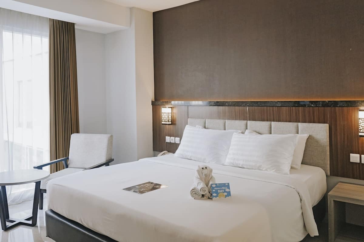 A hotel room with a large bed, a bedside table, a chair, and a small table.