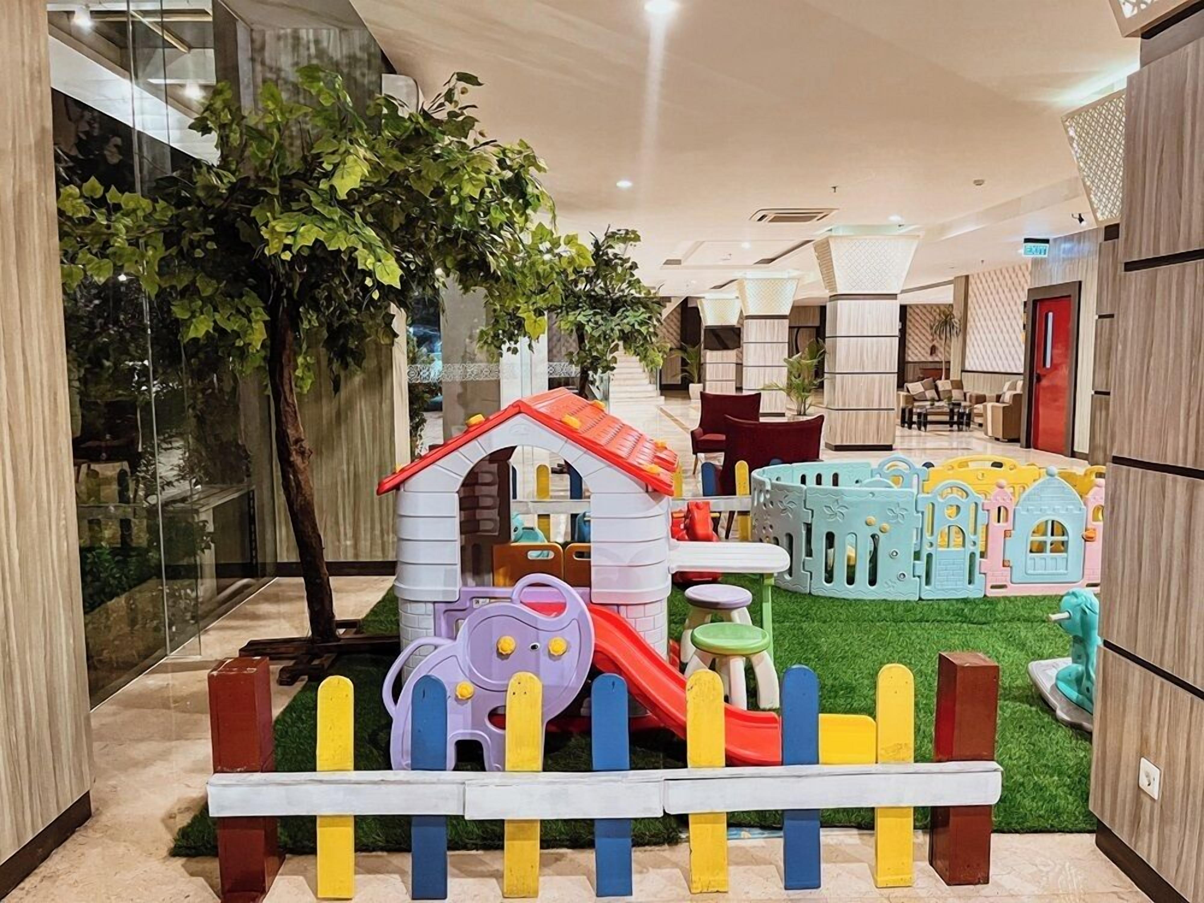 Un espace de jeux pour enfants avec un toboggan, des cabanes et un petit arbre.