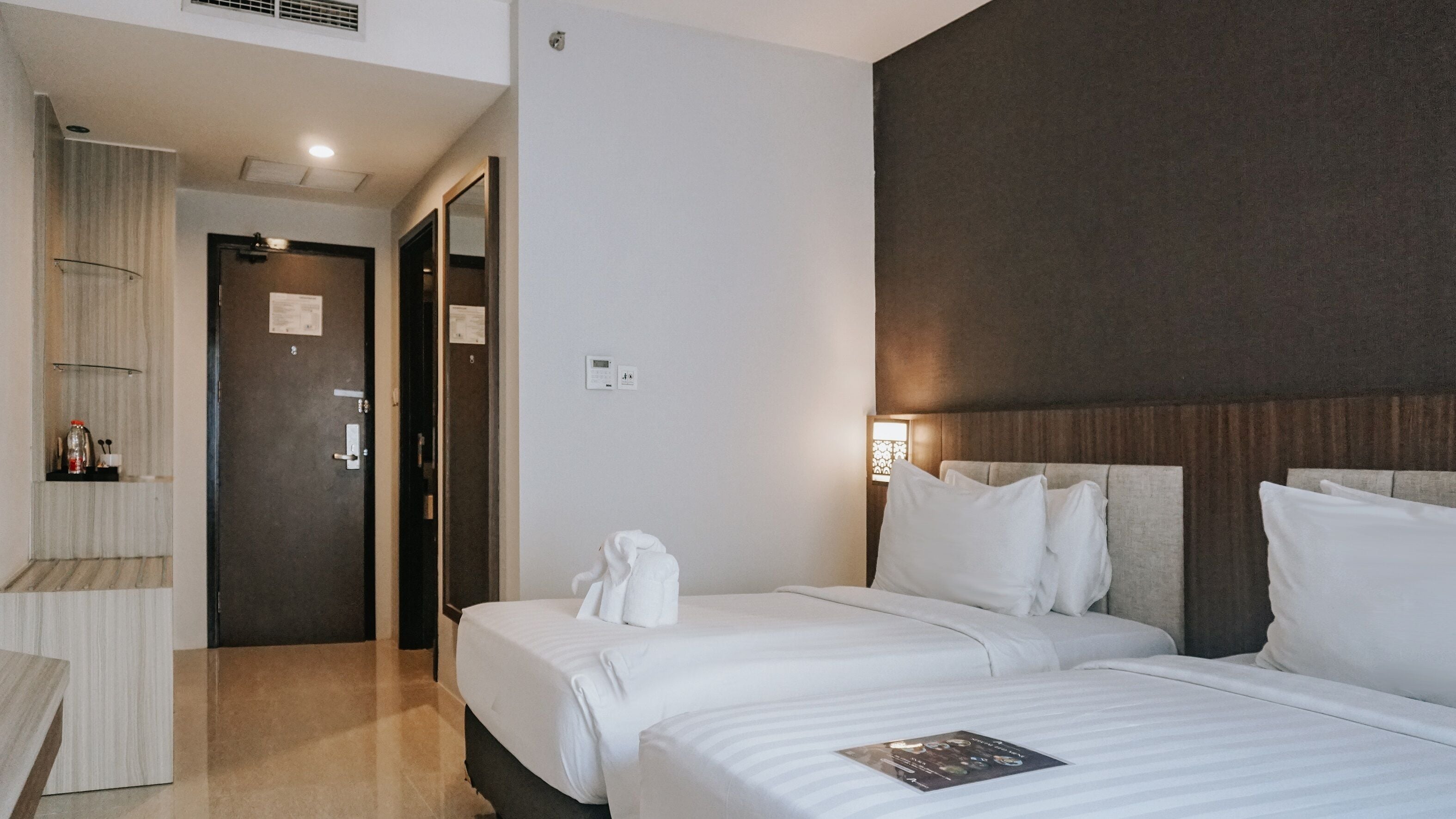A hotel room with two beds, a bathroom, and a hallway.
