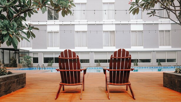 Two Adirondack chairs facing a swimming pool with a modern building in the background. - Ascent Premiere Pasuruan (Pasuruan)