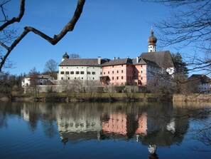 A large, multi-colored building with a prominent tower, reflecting in a calm body of water.