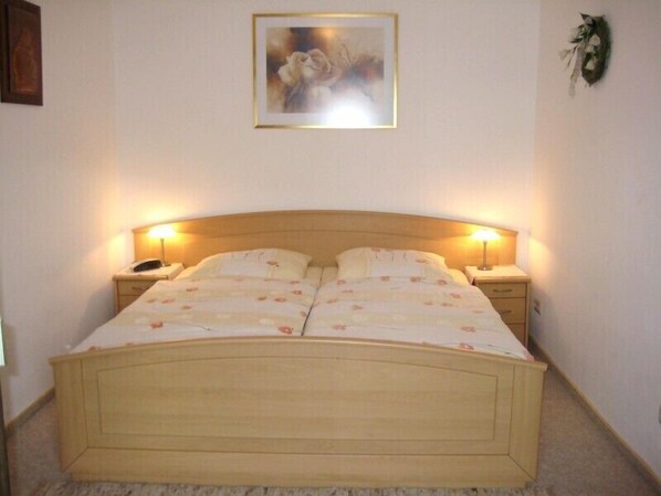 A bedroom with a wooden bed, two bedside tables with lamps, a framed picture on the wall, and a carpeted floor.