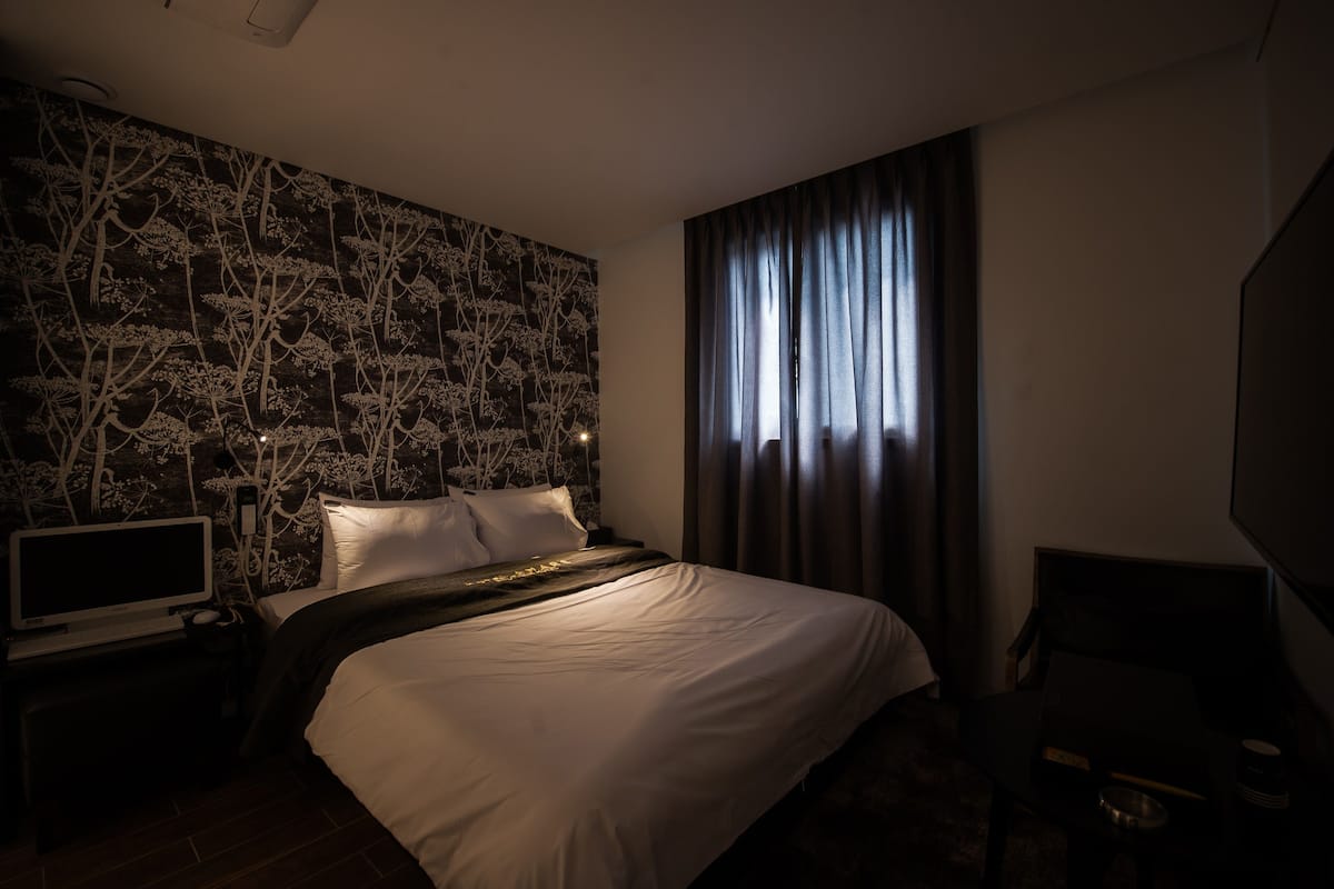 Une chambre d’hôtel avec un grand lit, un téléviseur à écran plat, un téléviseur fixé au mur et une fenêtre avec des rideaux.