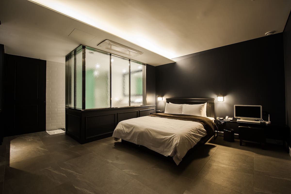 Une chambre moderne avec un lit, un bureau, un ordinateur et une fenêtre à vitrage dépoli.