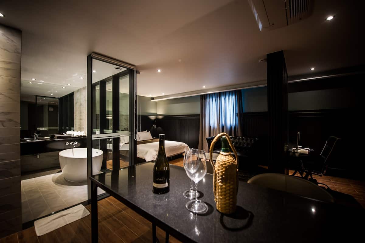 Une chambre d’hôtel moderne dotée d’un grand lit, d’une salle de bain séparée, d’un coin repas et offrant une vue sur le paysage urbain.