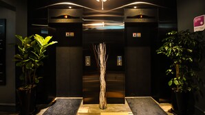 An elevator entrance with a modern design, featuring a central decorative element and potted plants on either side. - Hotel AMARE (Suwon)
