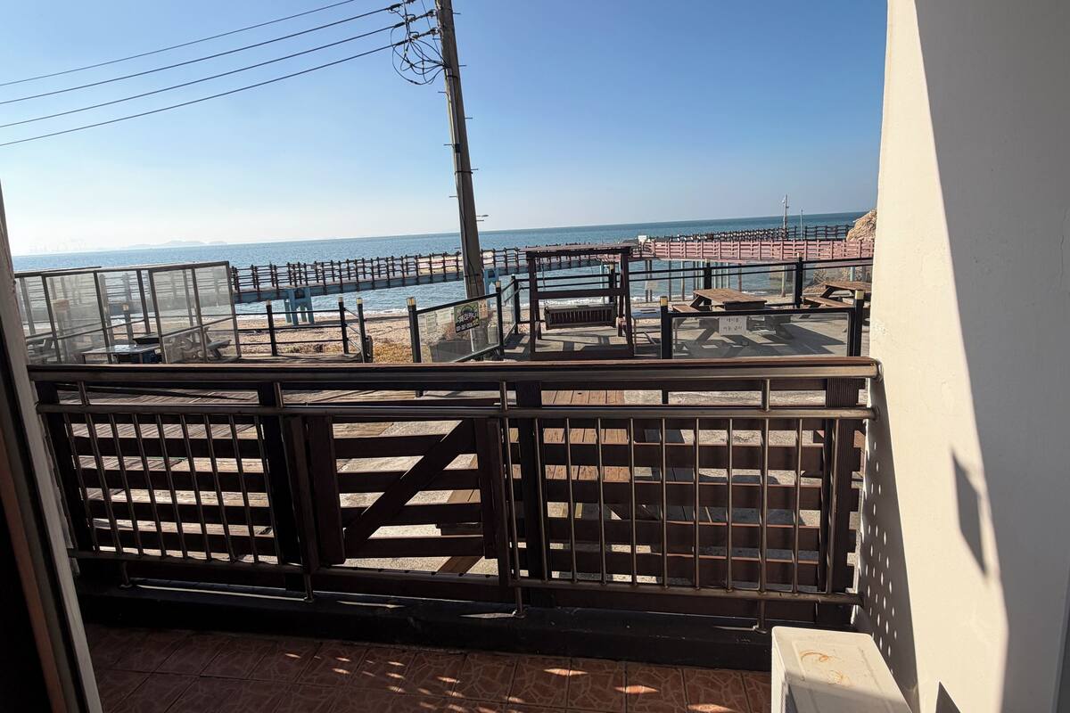 A balcony with a view of a beach, wooden deck, and a wooden fence.