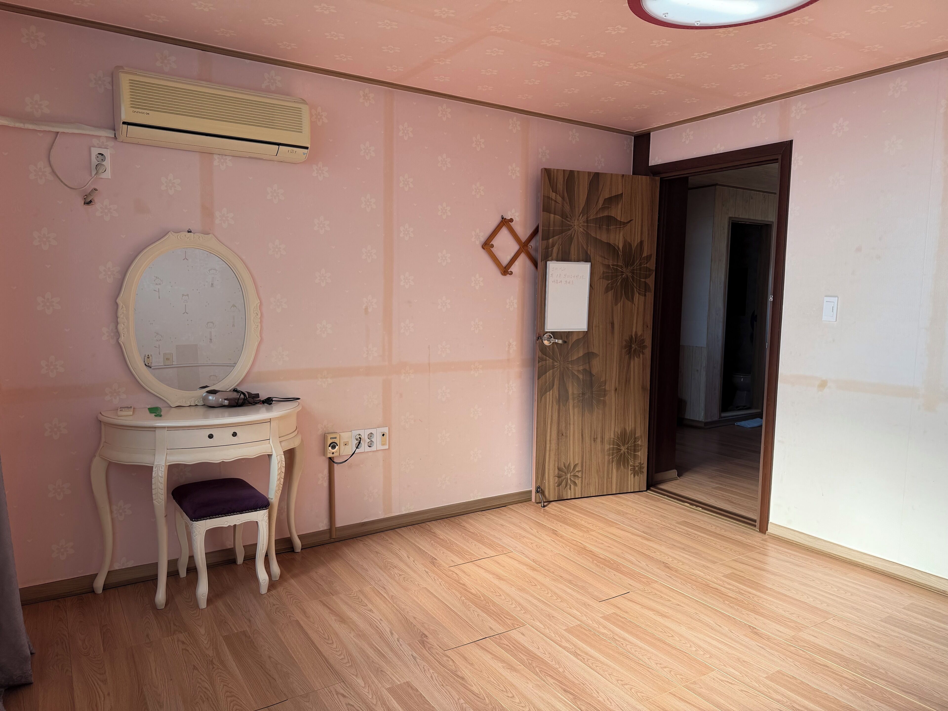 Une pièce avec un plancher en bois, une coiffeuse avec un miroir, un climatiseur et une porte dotée d’un miroir.