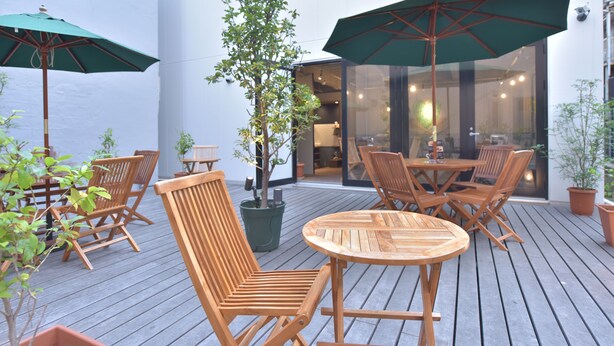 An outdoor patio with wooden furniture, green umbrellas, and potted plants. - Chillulu Coffee & Hostel (Yokohama)