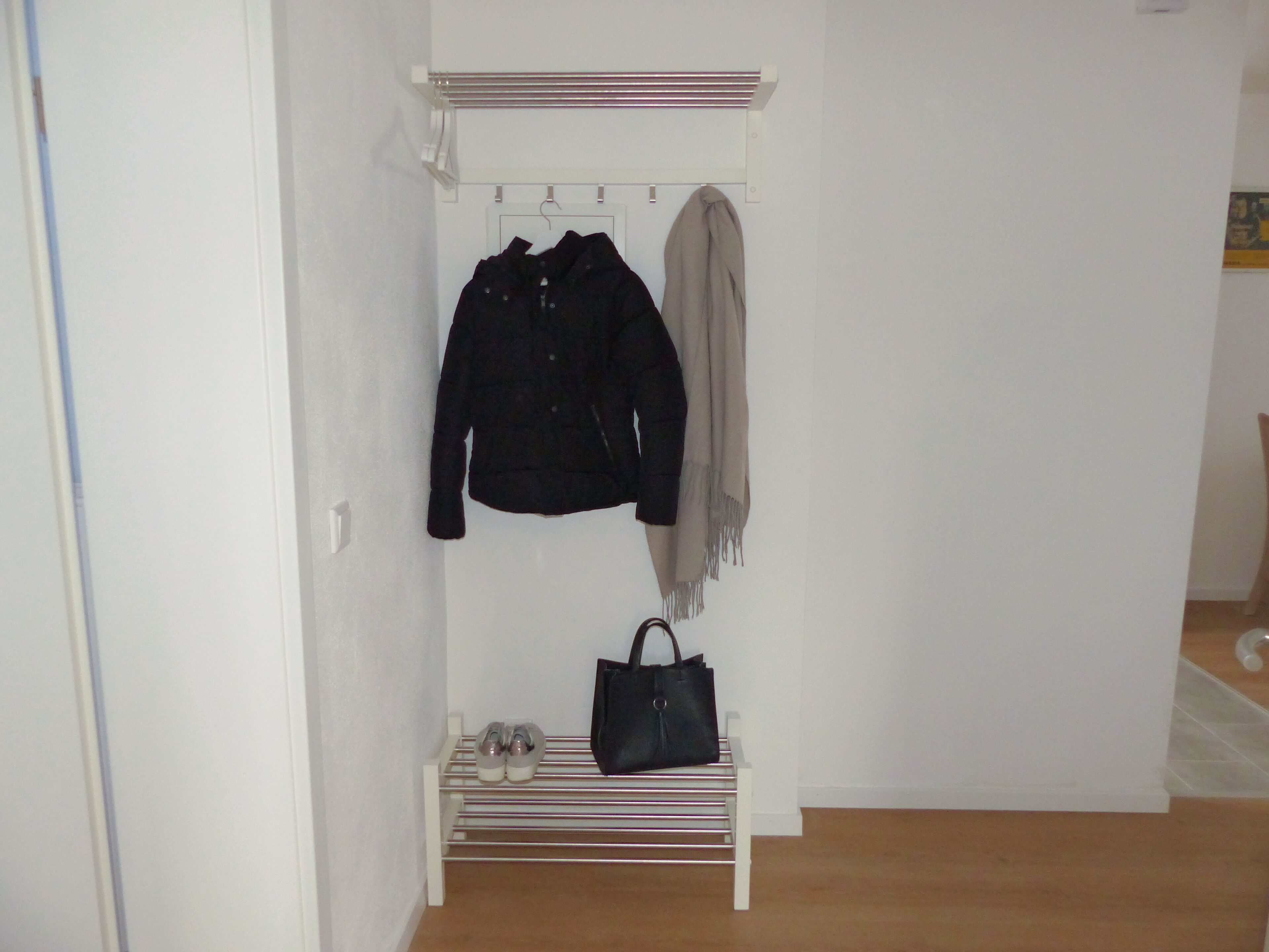 Ein kleiner, weißer, an der Wand befestigter Schrank mit Kleiderstange, Ablagefläche und Schuhablage.