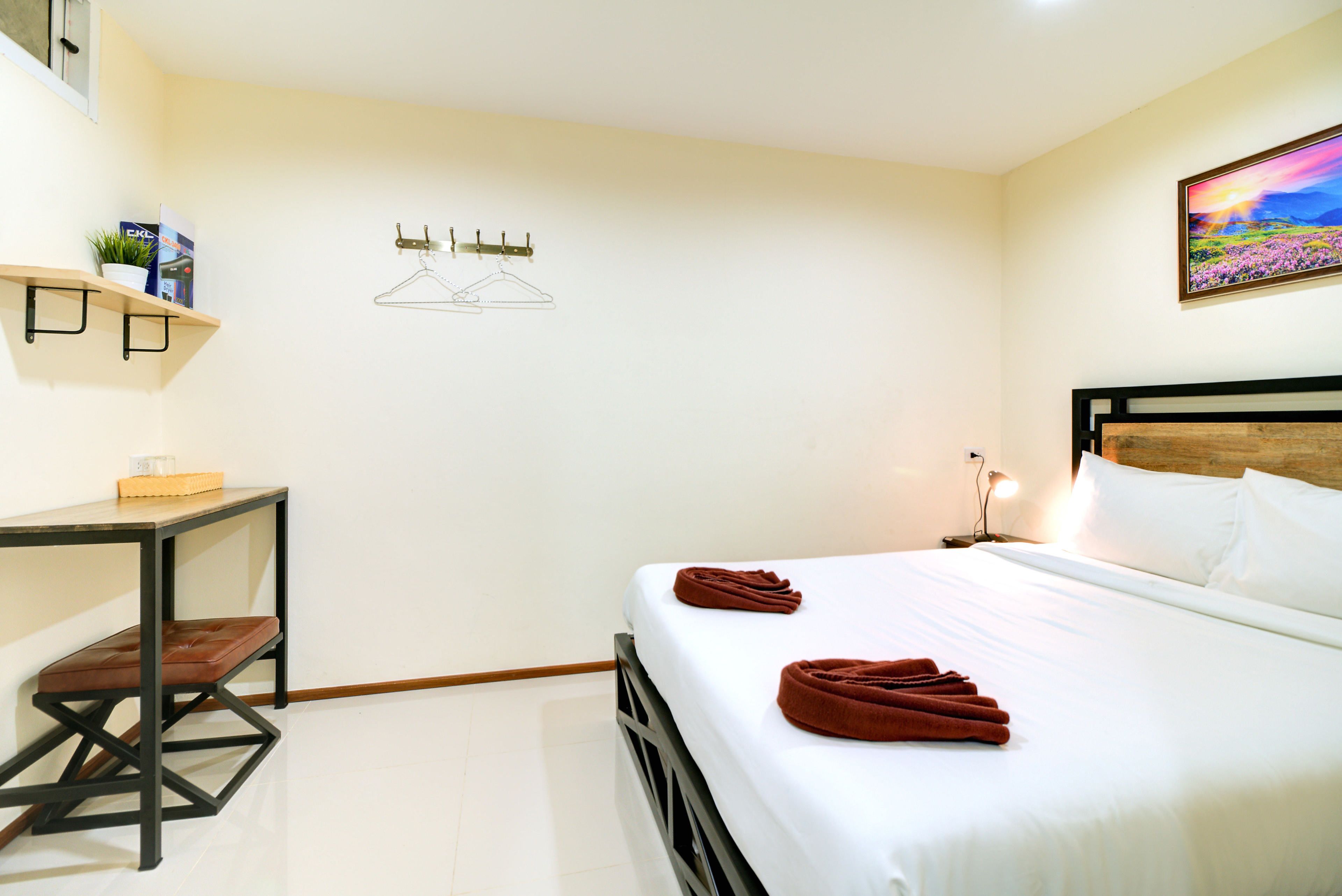 A hotel room with a bed, a desk, a shelf with a plant, and a wall-mounted hanger.