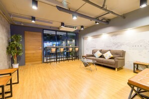 Um espaço de escritório moderno com piso de madeira, um sofá marrom com almofadas, uma mesa de centro de vidro e um mapa na parede.