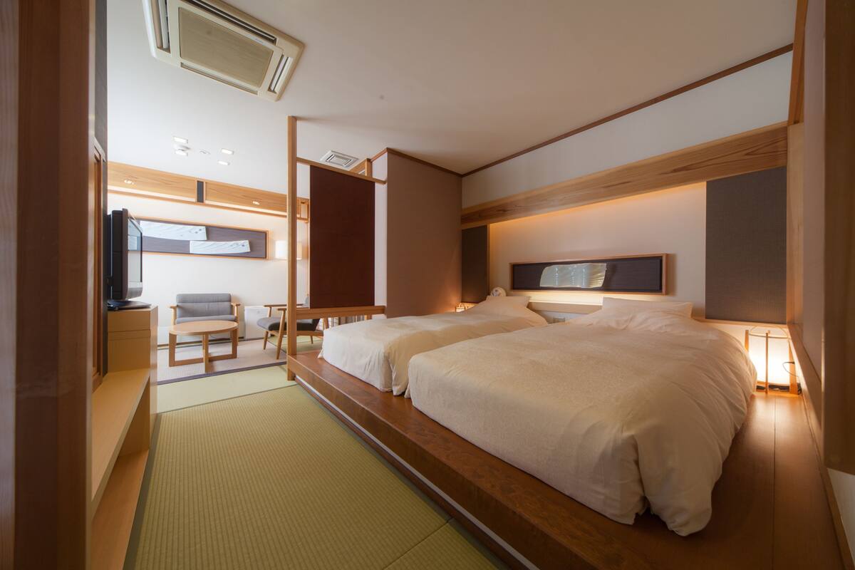 A hotel room with a bed, bedside tables, a TV, a sofa, and a desk.