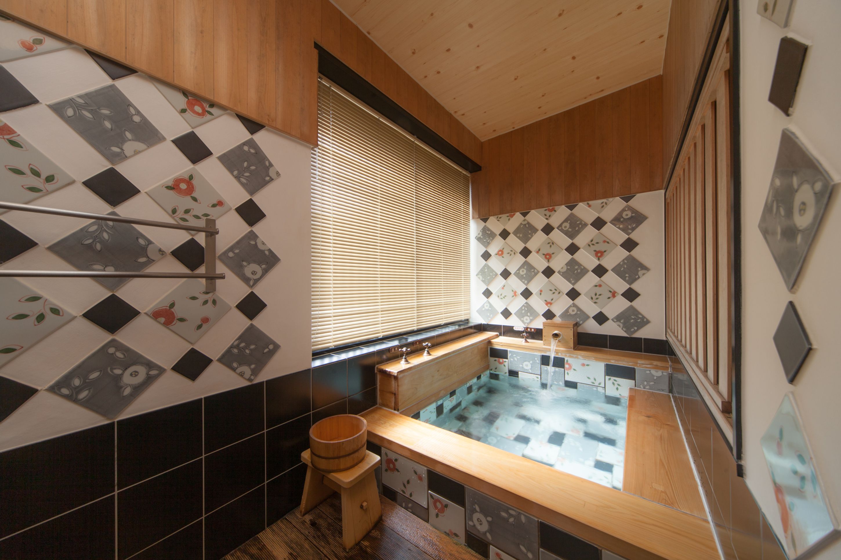 Ein modernes Badezimmer mit einer Holzbadewanne, schwarz-weißen Fliesen und einer hölzernen Sitzbank.