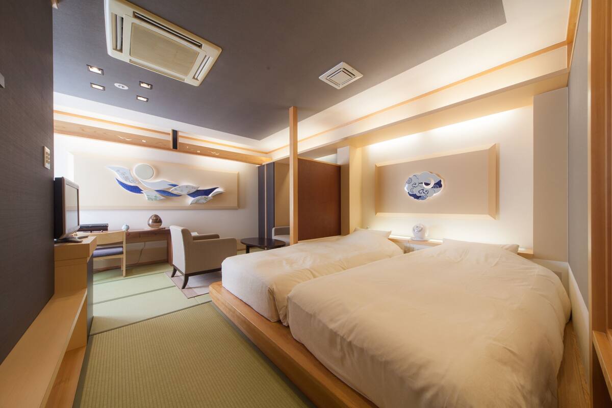 A hotel room with two beds, a desk, a chair, and a large window.