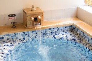 Relax in a hot tub with a mosaic floor and a nearby cabinet.