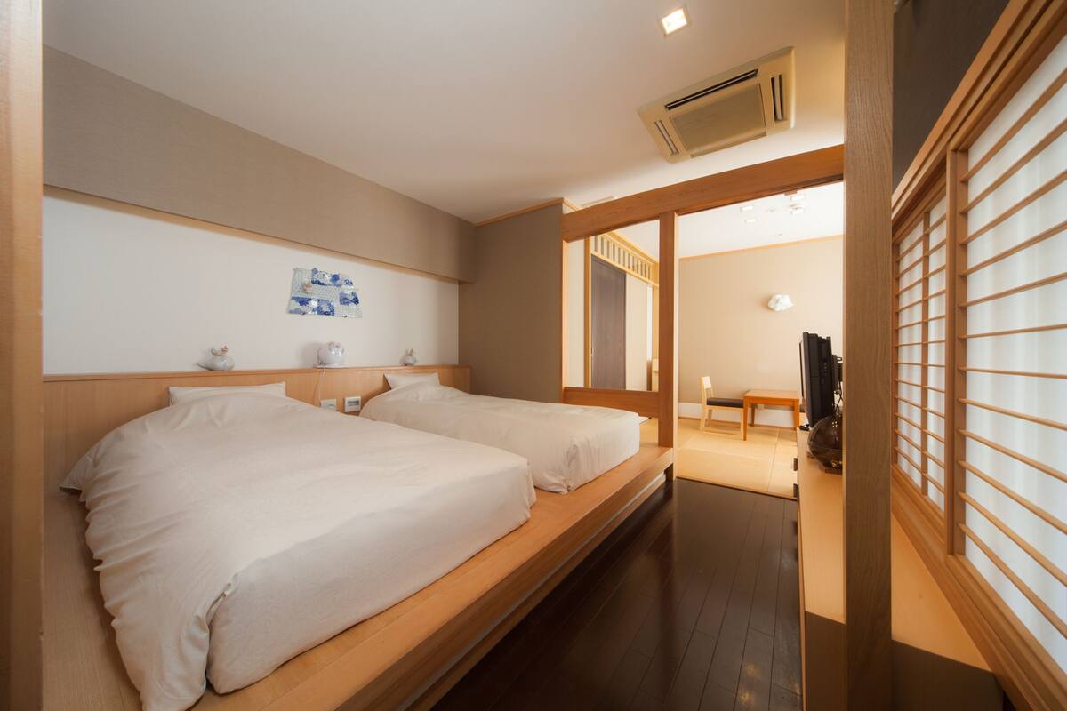 A hotel room with two beds, a wooden floor, a small table, and a TV.
