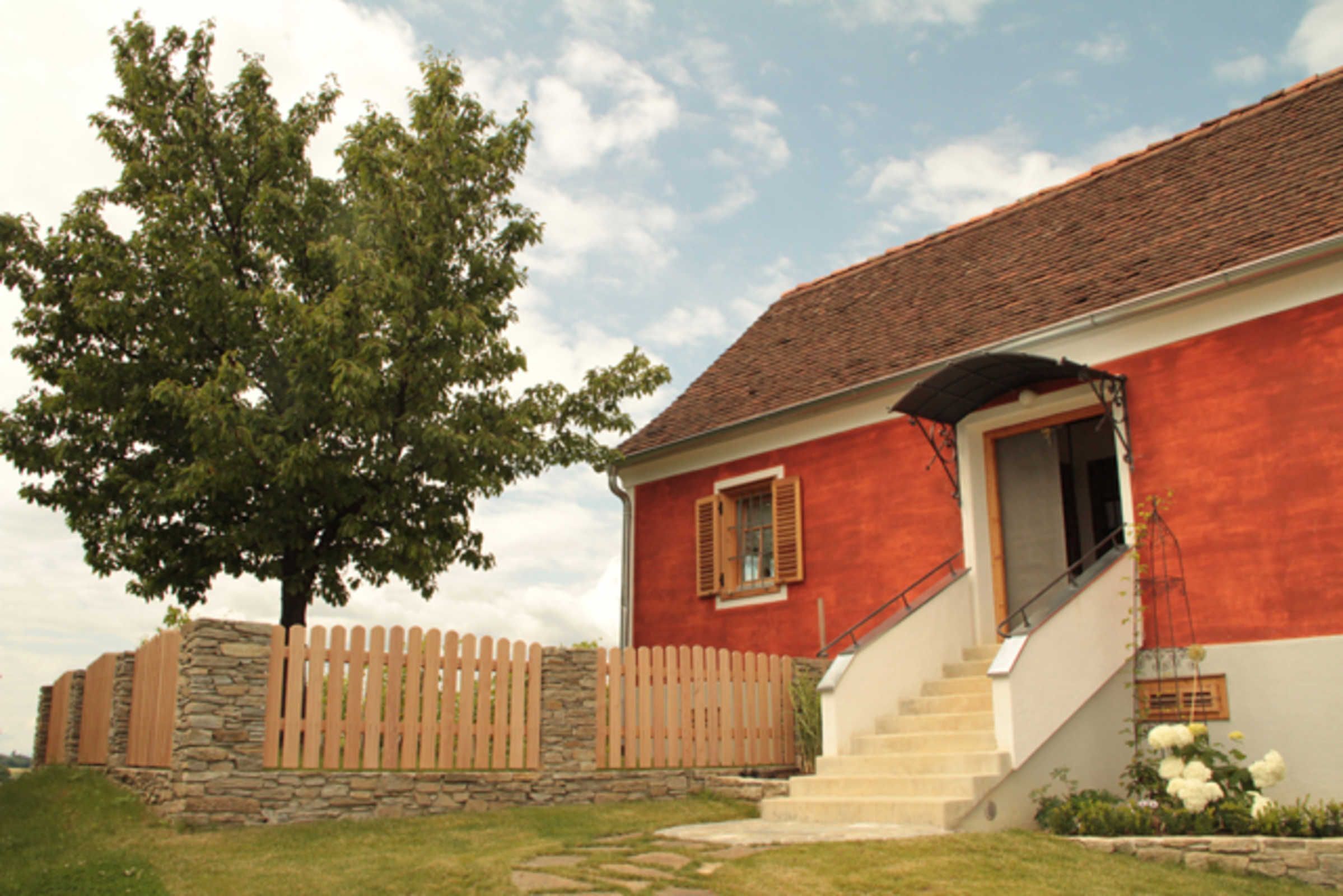 A red building with a stone wall, wooden fence, and a staircase leading to the entrance.