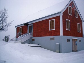 Un edificio rojo y blanco con una escalera que conduce a la entrada, rodeado de nieve.