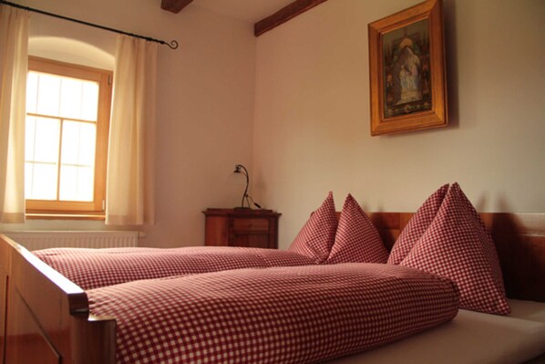 Un dormitorio con cama, ventana con cortinas, mesita de noche y un cuadro enmarcado en la pared.