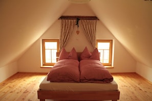 A bedroom with a sloped ceiling, two windows, a bed with checkered bedding, and a heart-shaped decoration.
