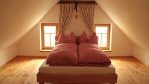 A bedroom with a sloped ceiling, two windows, a bed with checkered bedding, and a heart-shaped decoration.