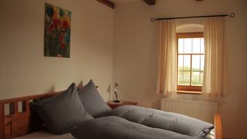 A bedroom with a bed, a nightstand, a window with curtains, a radiator, and a painting on the wall.