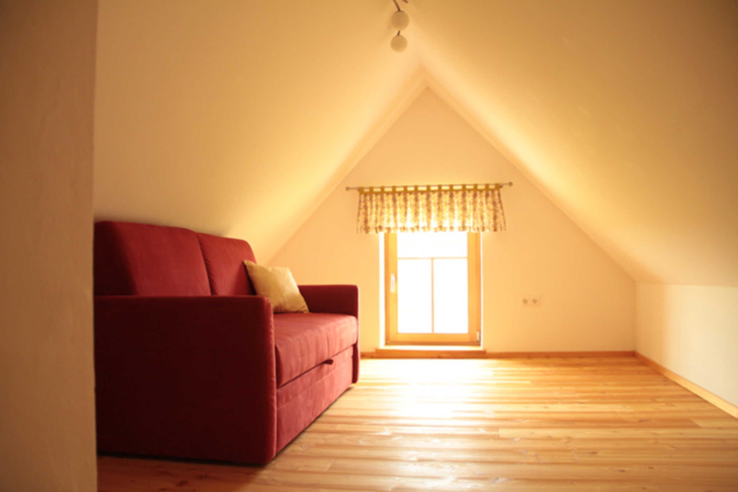 An empty room with a red sofa, a window with a valance, and wooden flooring.