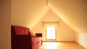 An empty room with a red sofa, a window with a valance, and wooden flooring.
