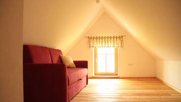 An empty room with a red sofa, a window with a valance, and wooden flooring.