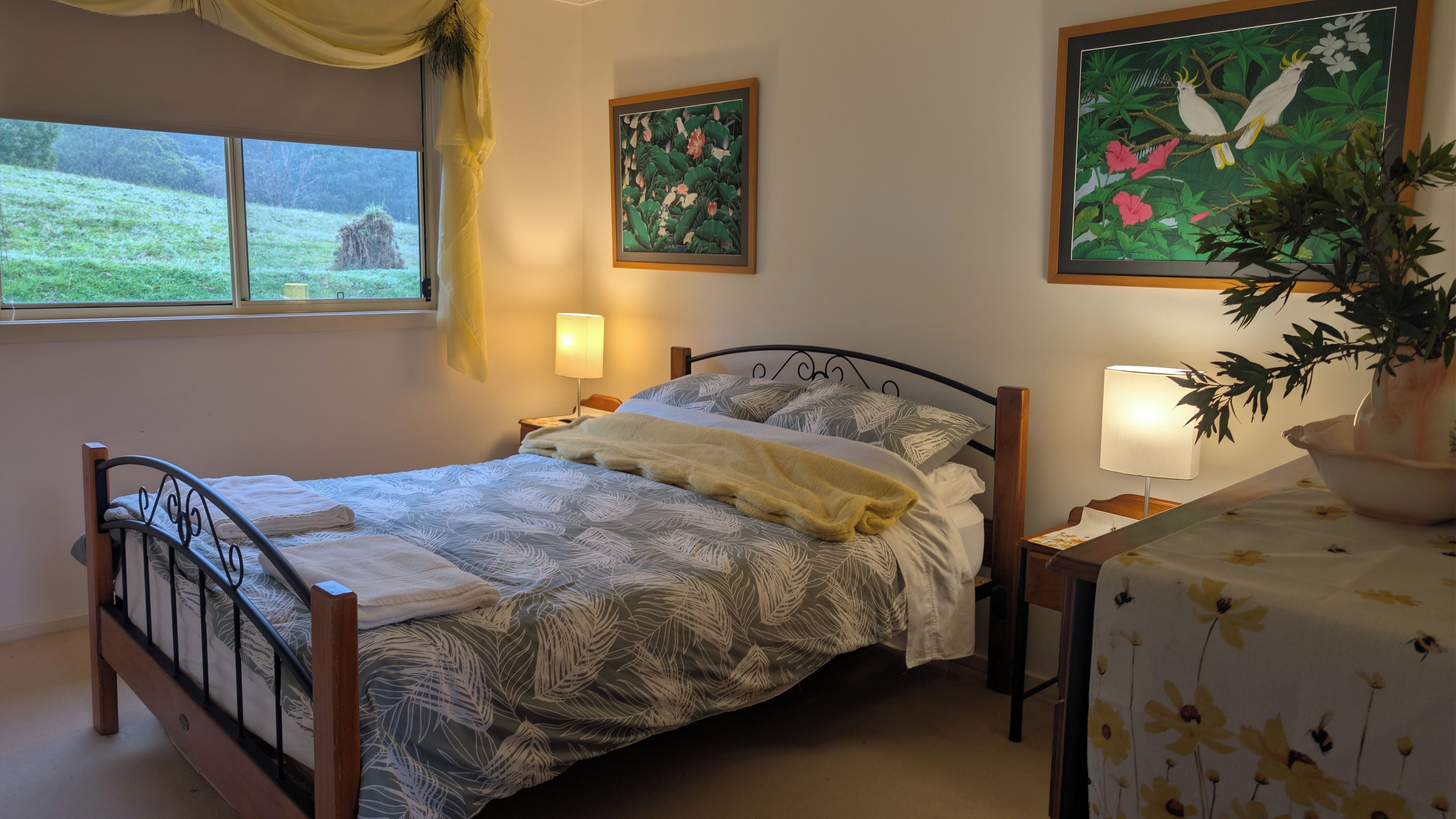 A bedroom with a bed, bedside lamps, a window with curtains, and a painting on the wall.