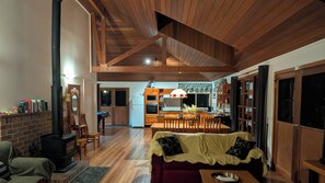 A spacious living area with a fireplace, wooden furniture, and a kitchen in the background. - Blackwattle at Barrington Tops (Bandon Grove)