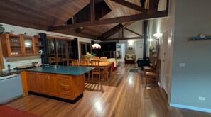 A spacious kitchen with wooden cabinets, a central island, and a dining area with wooden chairs. - Blackwattle at Barrington Tops (Bandon Grove)