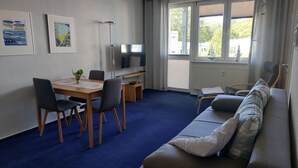 A living room with a sofa, a TV, a dining table with chairs, and artwork on the wall.