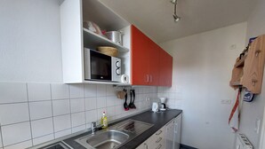 A kitchen with a microwave, oven, and sink. There are cabinets, a countertop, and a radiator.