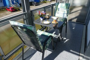 A balcony with a table set for two, chairs, a vase with flowers, and a red car parked outside. - Damerow Dünenstraße - Holiday apartment (Zinnowitz)