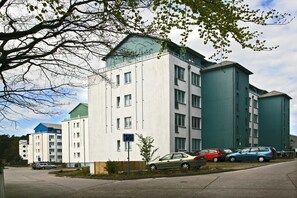 A multi-story building with a parking area in front. - Damerow Dünenstraße - Holiday apartment (Zinnowitz)