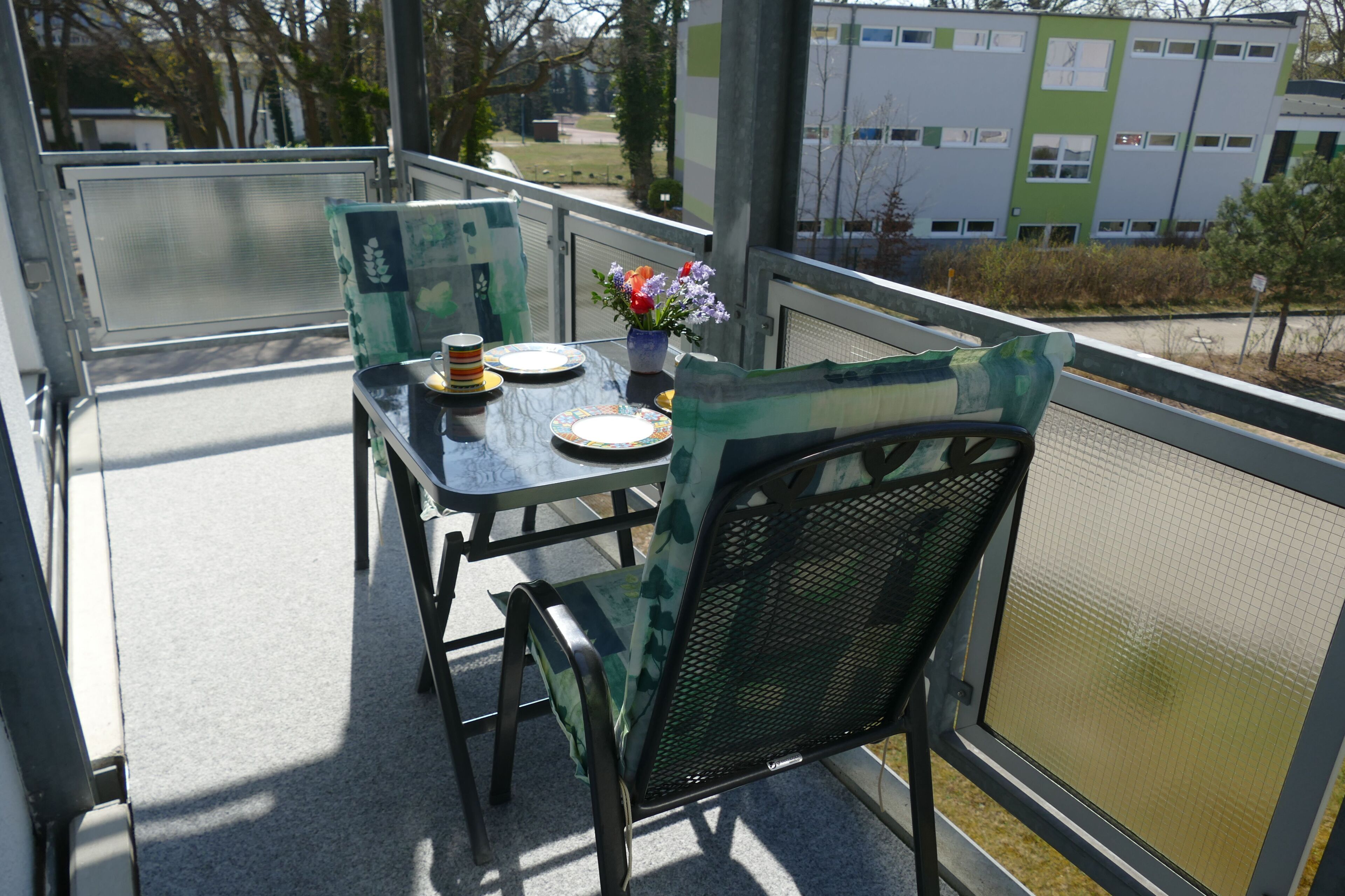 A balcony with a table, chairs, and a vase of flowers.