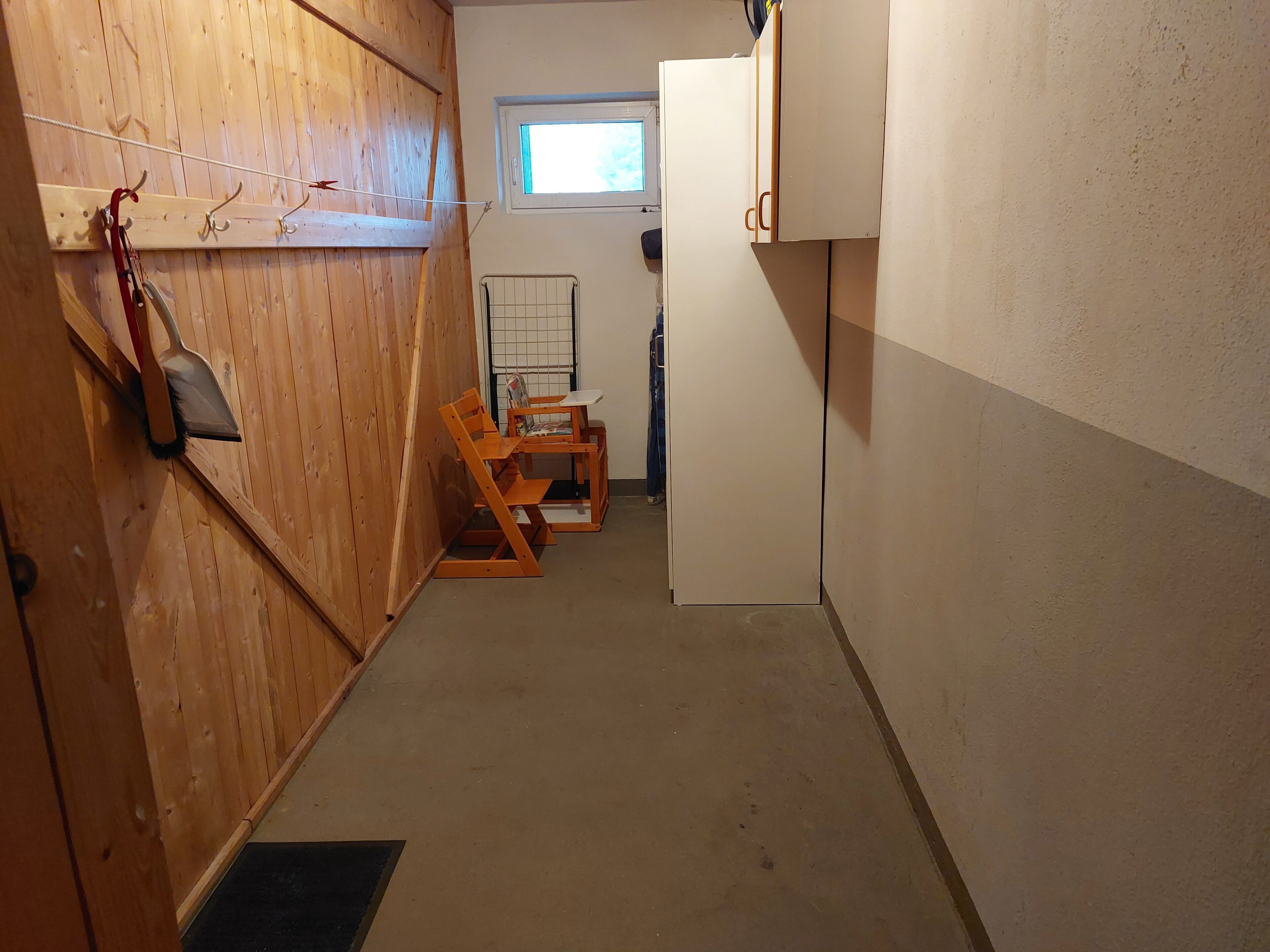 A narrow hallway with wooden walls, a window, a radiator, and a door leading to a room.
