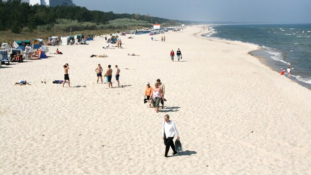 A beach with people walking, tents, and a building in the background.