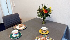A dining table with a vase of flowers, a chair, and a plate with a piece of cake.