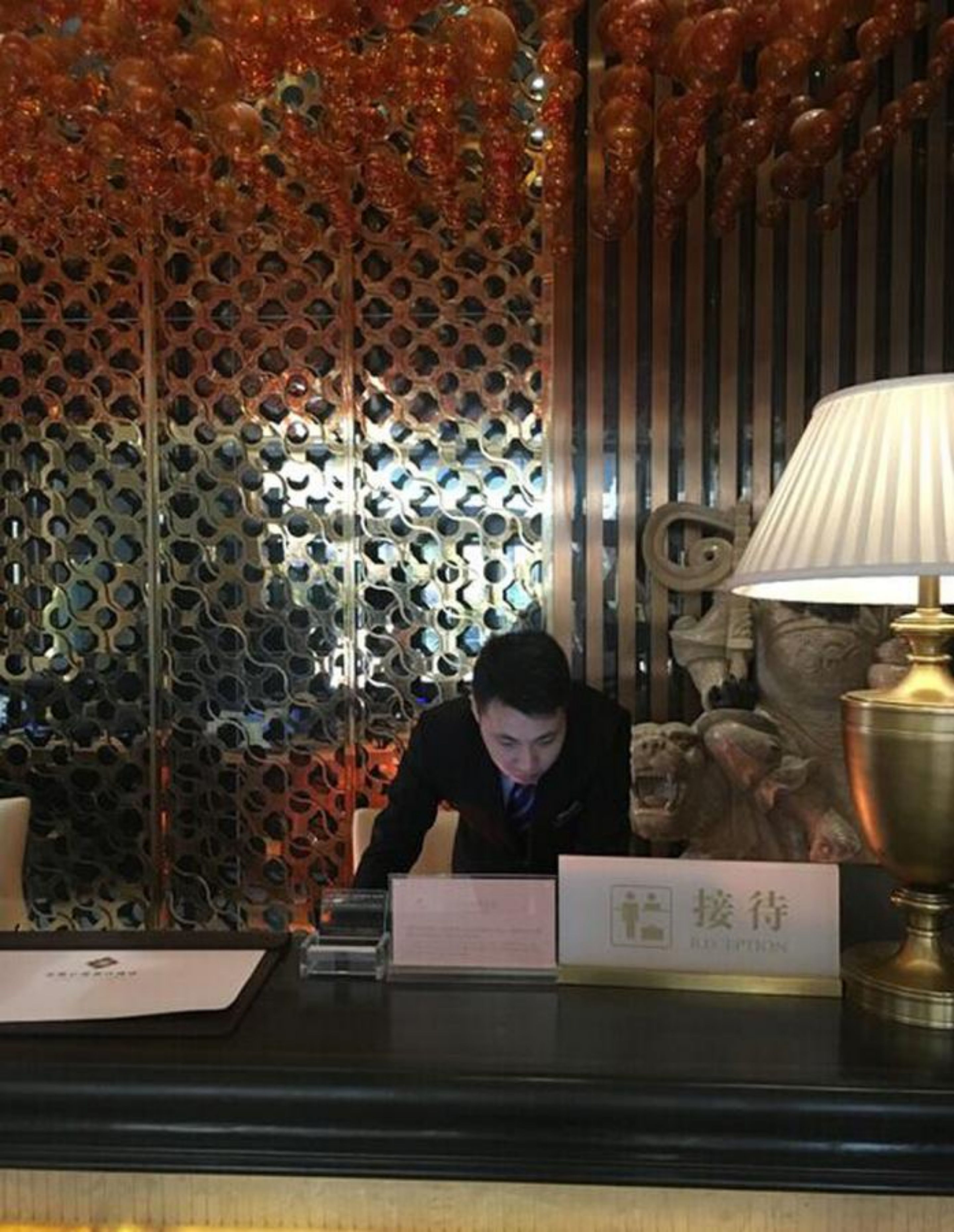 A reception desk with a decorative metal partition, a lamp, and a sign with Chinese characters.