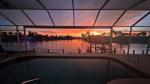 A pool area with a view of a sunset over water, palm trees, and a dock. - Fantastic villa with an fantastic view in a quiet location - Villa Wonderview (Cape Coral)