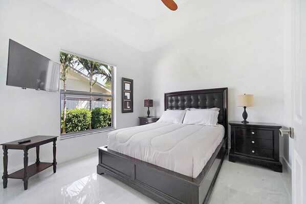 A bedroom with a bed, bedside tables, a TV, and a window with a view of greenery.