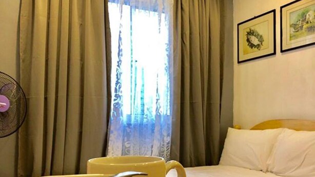 A hotel room with a bed, a table with a cup and saucer, and curtains. - Umali Kayo at Megatower Residences 1 (Baguio)